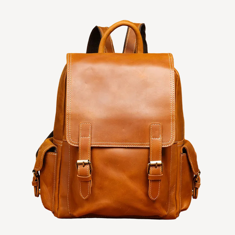 A brown leather backpack with dual top handles, buckle details, and side pockets, set against a warm brown textured background with vintage props.