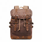 A brown waxed canvas backpack with tan leather straps and metal snap closures, shown against a plain white background 