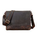 A dark brown distressed leather messenger bag with a wide adjustable shoulder strap and a gold-tone buckle, displayed on a wooden surface with a neutral gray background.